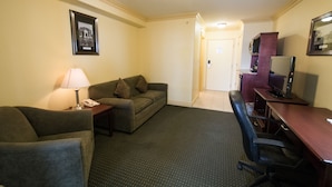 A hotel room with a sofa, a desk with a computer, a lamp, and a framed picture on the wall. - Nova Inn Peace River (Peace River)