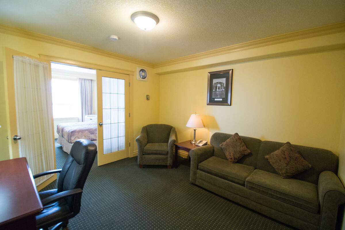 A hotel room with a bed, a desk, a chair, a sofa, and a lamp.