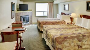 A hotel room with two beds, a television, a fireplace, a dining area with a table and chairs, and a window with curtains. - Nova Inn Peace River (Peace River)