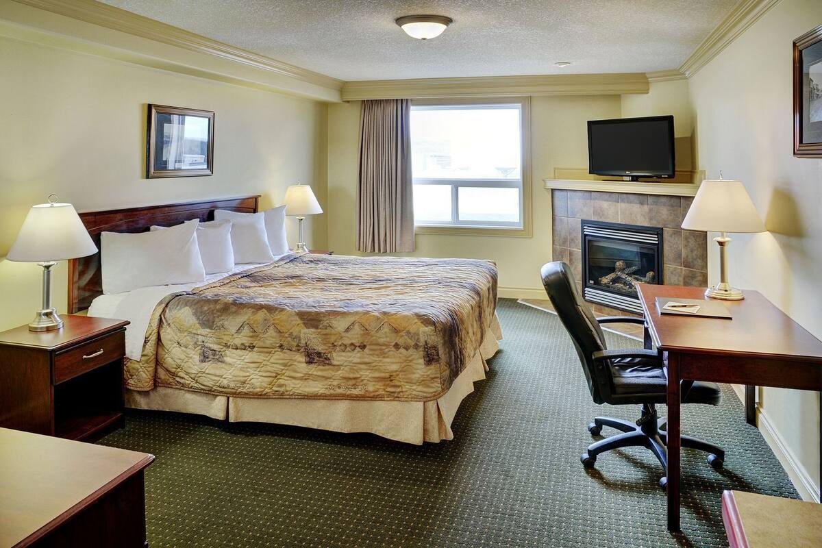 A hotel room with a bed, desk, chair, television, fireplace, and two lamps.