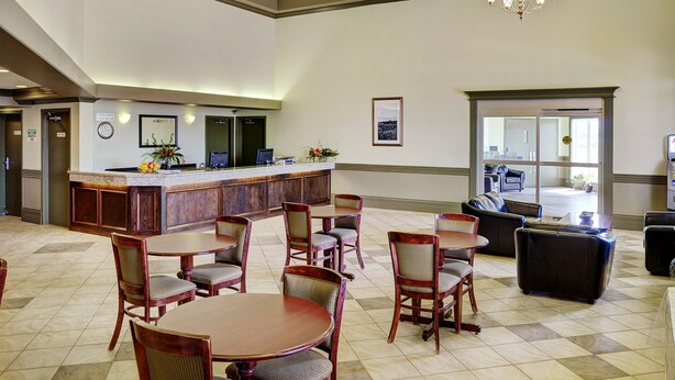 A hotel lobby with a reception desk, seating area, and a view of the outdoor patio. - Nova Inn Peace River (Peace River)