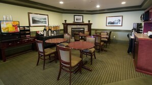 A hotel lobby with multiple round tables and chairs, a fireplace, framed pictures on the walls, and a bar area with a television. - Nova Inn Peace River (Peace River)