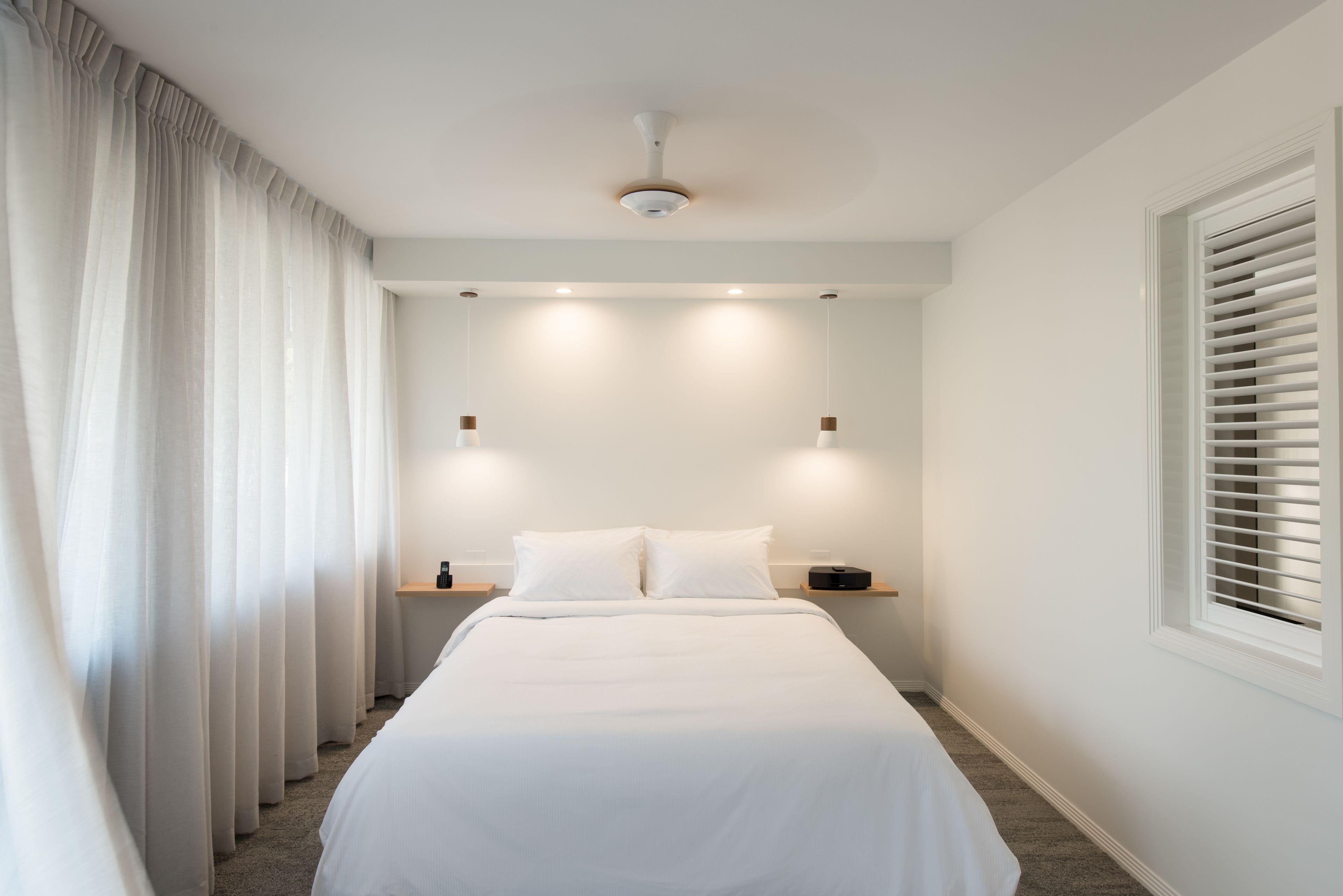 A modern bedroom with a large bed, a ceiling light, and a window with blinds.