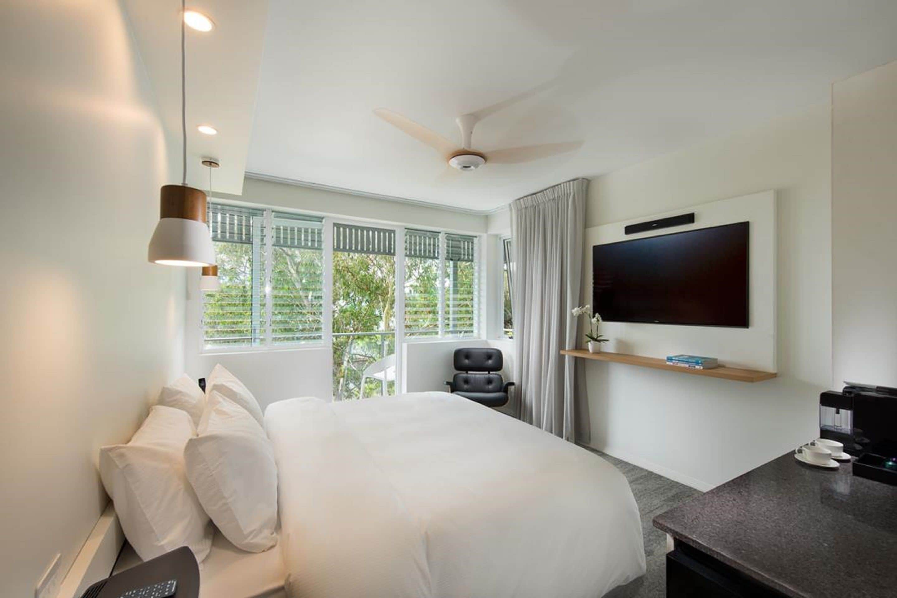 A hotel room with a bed, a desk, a television, a ceiling fan, and a window with curtains.