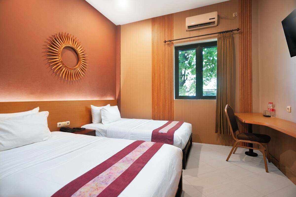 Habitación de hotel con dos camas, un escritorio, una silla, un televisor y una ventana con cortinas.