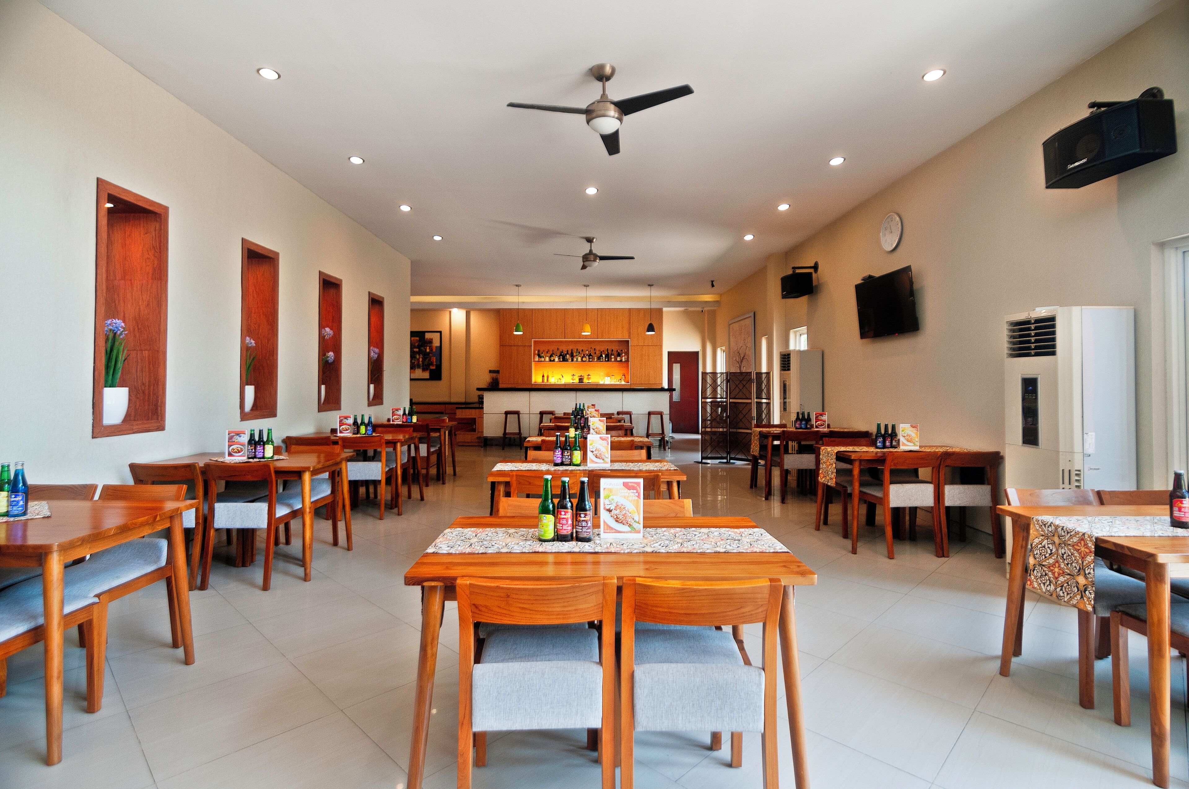 A spacious dining area with multiple wooden tables and chairs, ceiling fans, recessed lighting, and a central counter with a menu.
