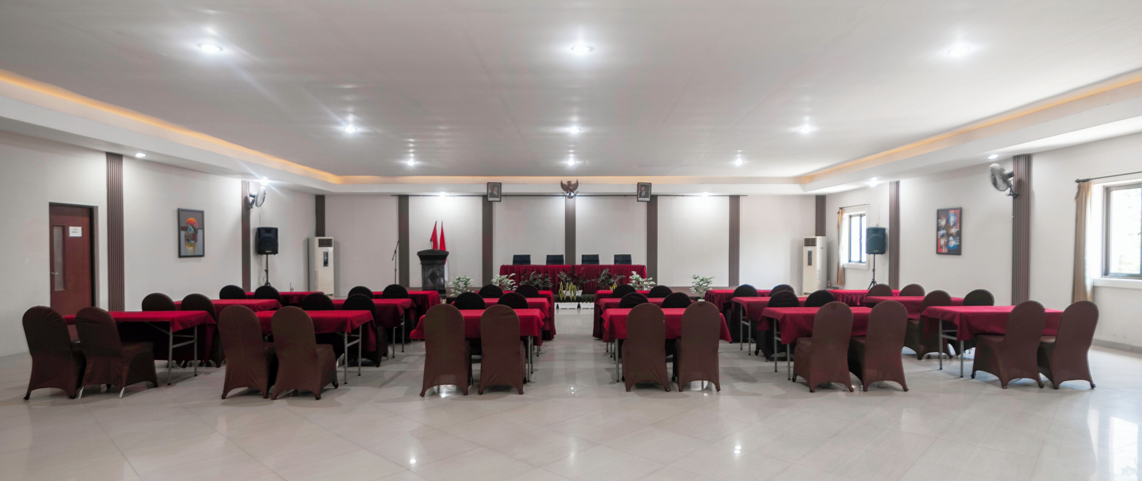 A conference room with rows of tables and chairs, a podium, and a stage with a backdrop.