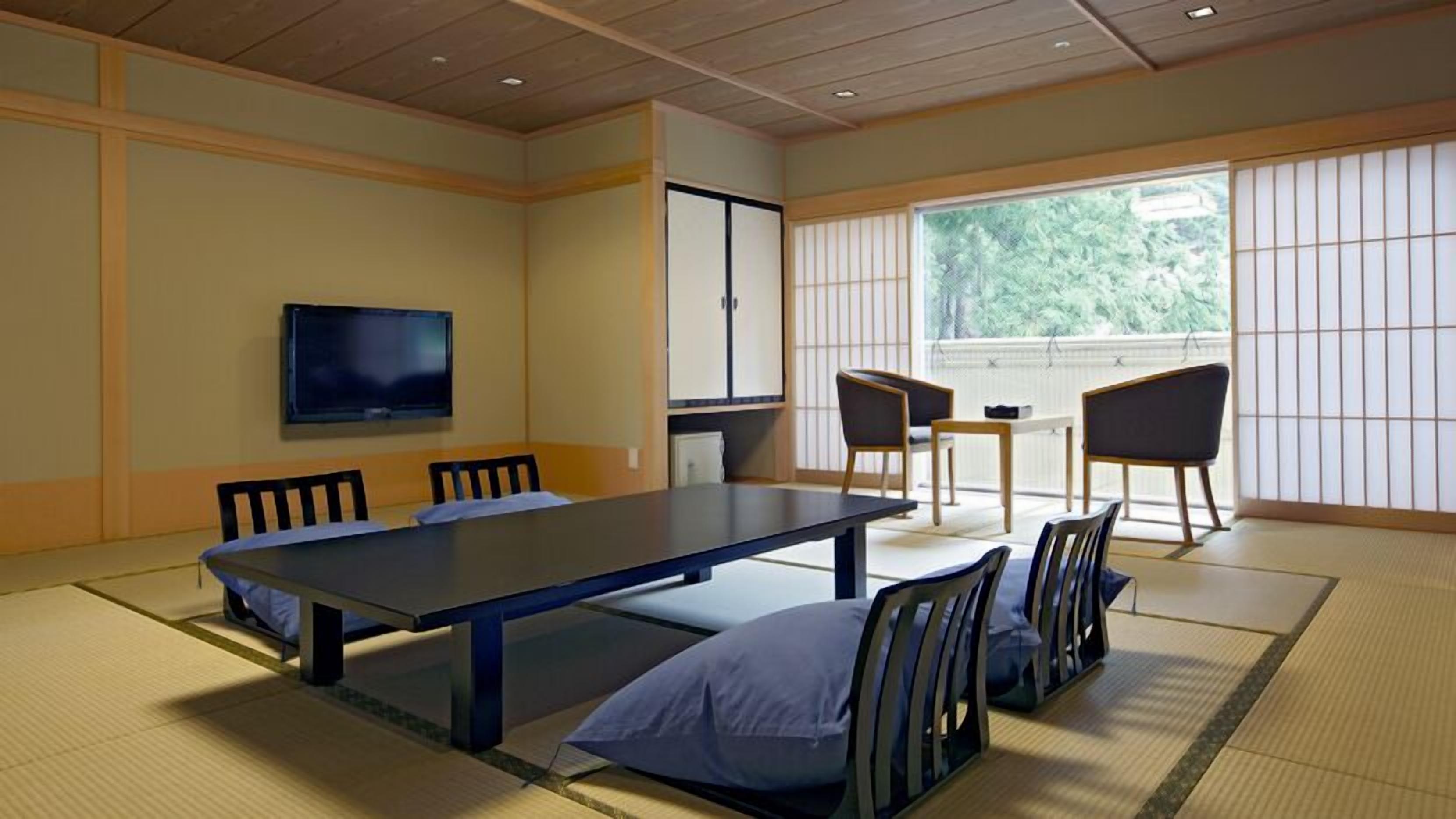 Um quarto japonês tradicional com tatames, uma mesa baixa, cadeiras, uma televisão e uma porta deslizante.