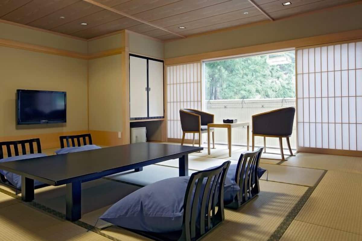 Una habitación japonesa tradicional con suelo de tatami, una mesa baja, sillas, un televisor y una puerta corredera.