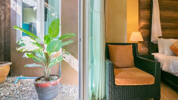 Una habitación con una silla de mimbre, una planta en maceta y una cama con dosel blanco.