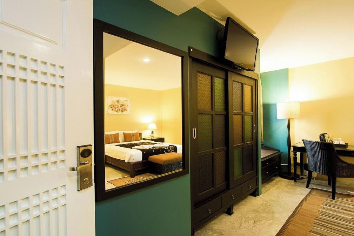 A hotel room with a large mirror reflecting the bed and a desk area with a chair and lamp.