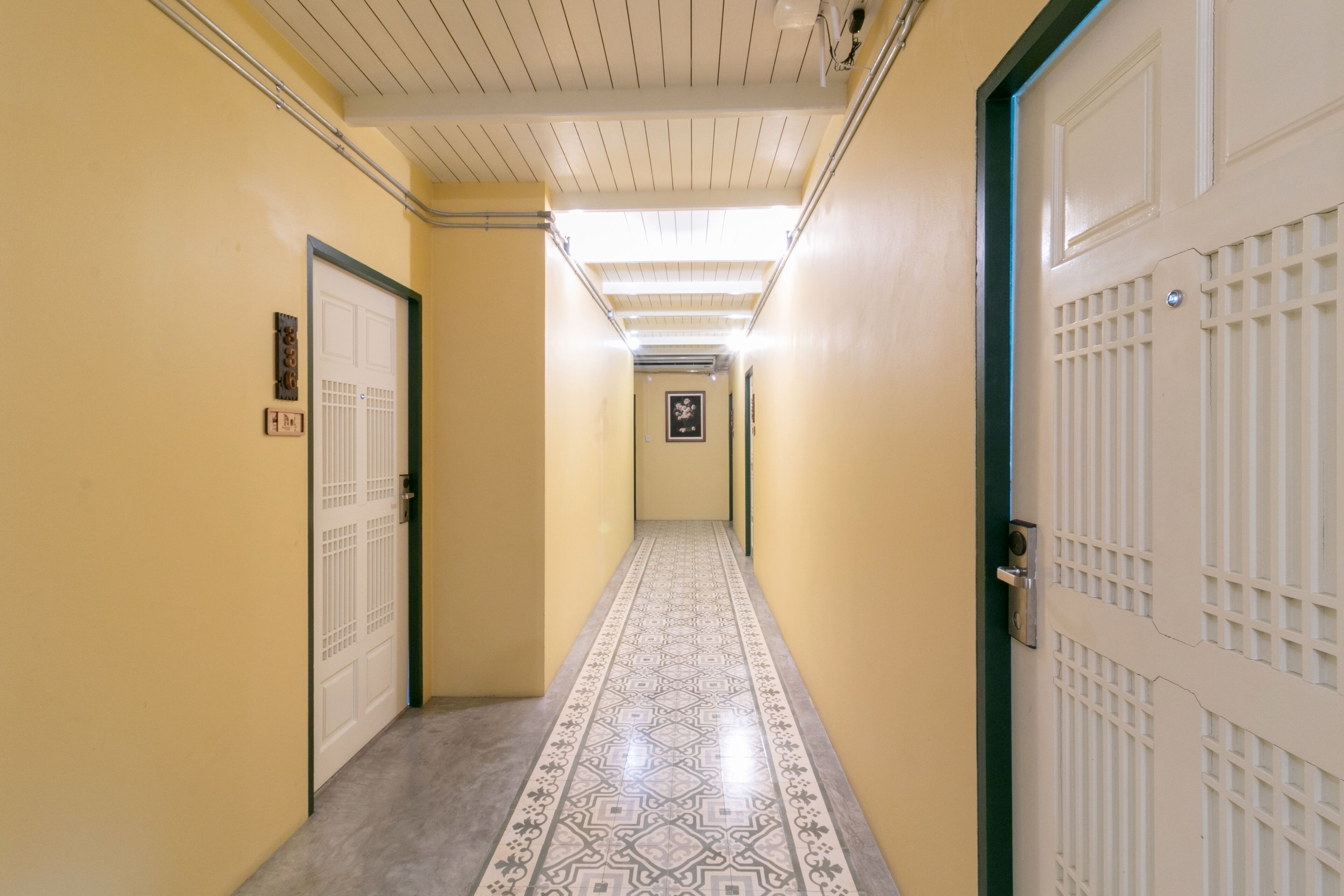 A hallway with patterned floor tiles, a white door with a metal handle, and a light fixture on the ceiling.