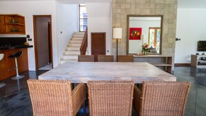 A spacious dining area with a large table and wicker chairs, a kitchen with wooden cabinets, and a staircase leading to an upper level. - Villa Martine (Seminyak)