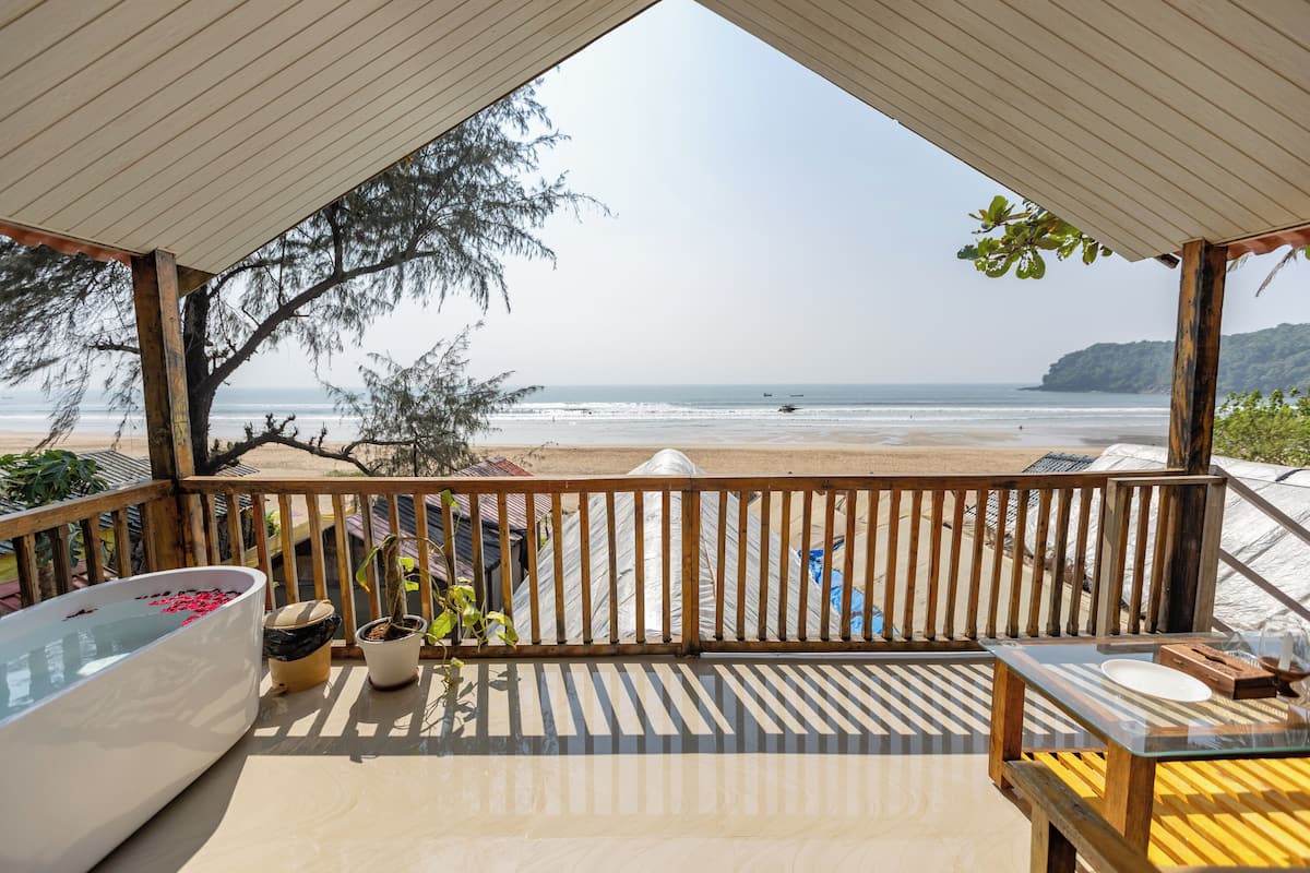 A wooden deck with a view of the beach, a bathtub with red flowers, and potted plants.