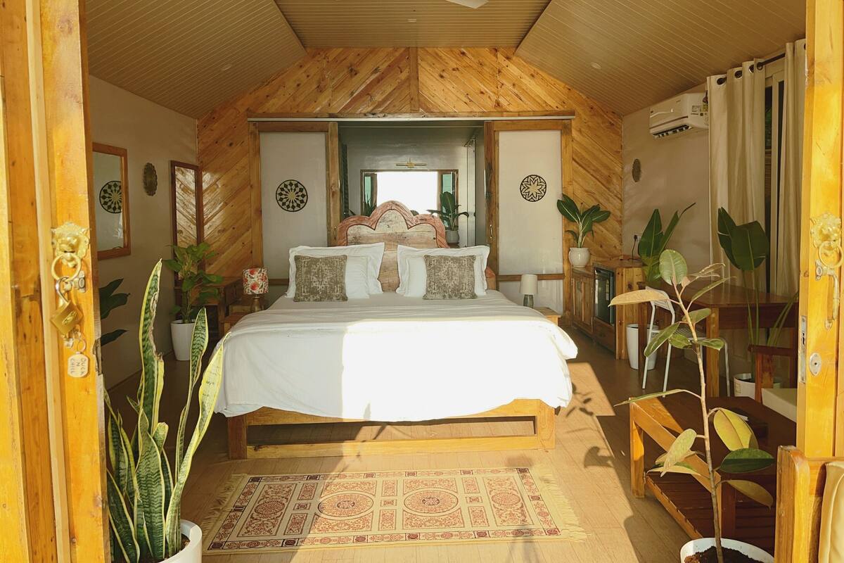 A wooden-paneled bedroom with a bed, two bedside tables, a ceiling fan, and several potted plants.