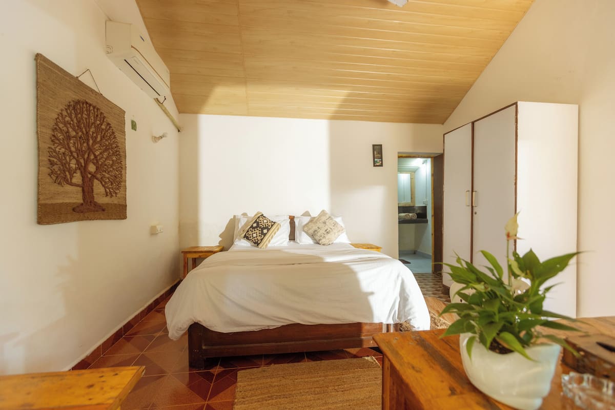 A bedroom with a wooden bed, a nightstand, a bedside table, a potted plant, and a wardrobe.