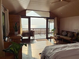 Una habitación con una cama grande, un escritorio de madera, una silla, una mesa y un balcón con vista al mar.