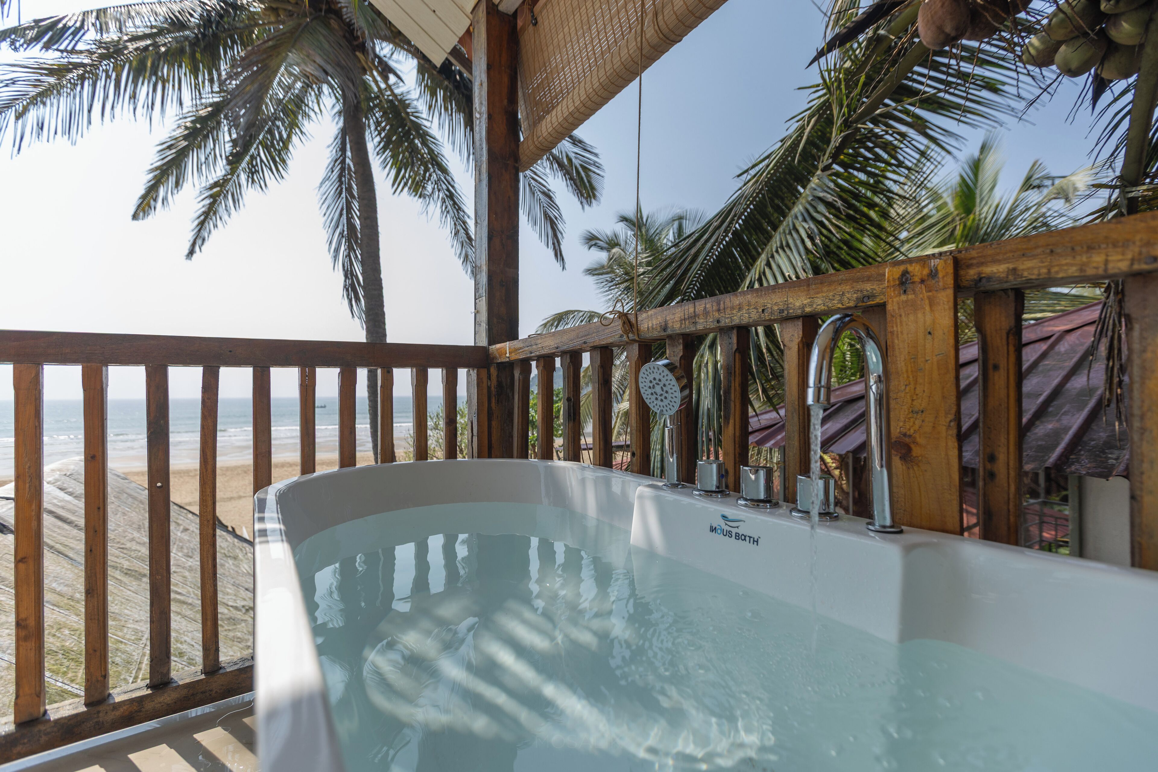 A hot tub on a wooden deck with a view of the beach and palm trees.