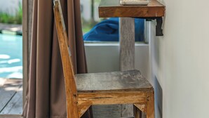 A wooden chair with a metal frame, a small table with a woven lamp, and a window with curtains. - Villa Laksmana Hideaway 2 (Seminyak)