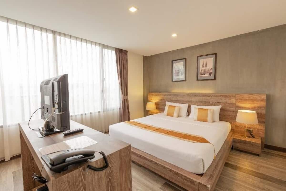 A hotel room with a bed, bedside lamps, a desk with a television, and a telephone.