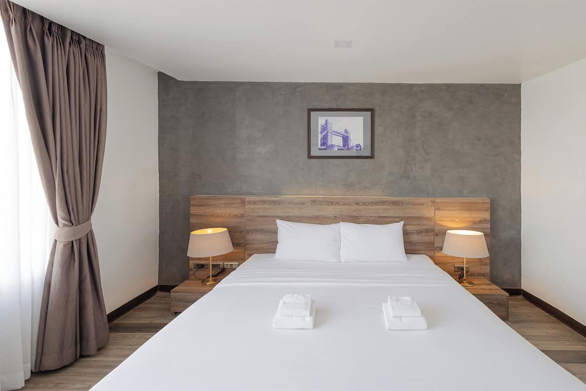 A hotel room with a large bed, two bedside lamps, a framed picture on the wall, and a pair of towels on the bed.