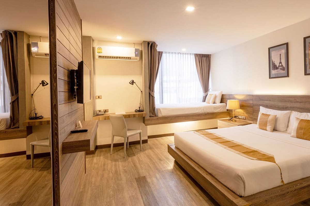 A hotel room with a large bed, a desk, a chair, a TV, and two windows with curtains.