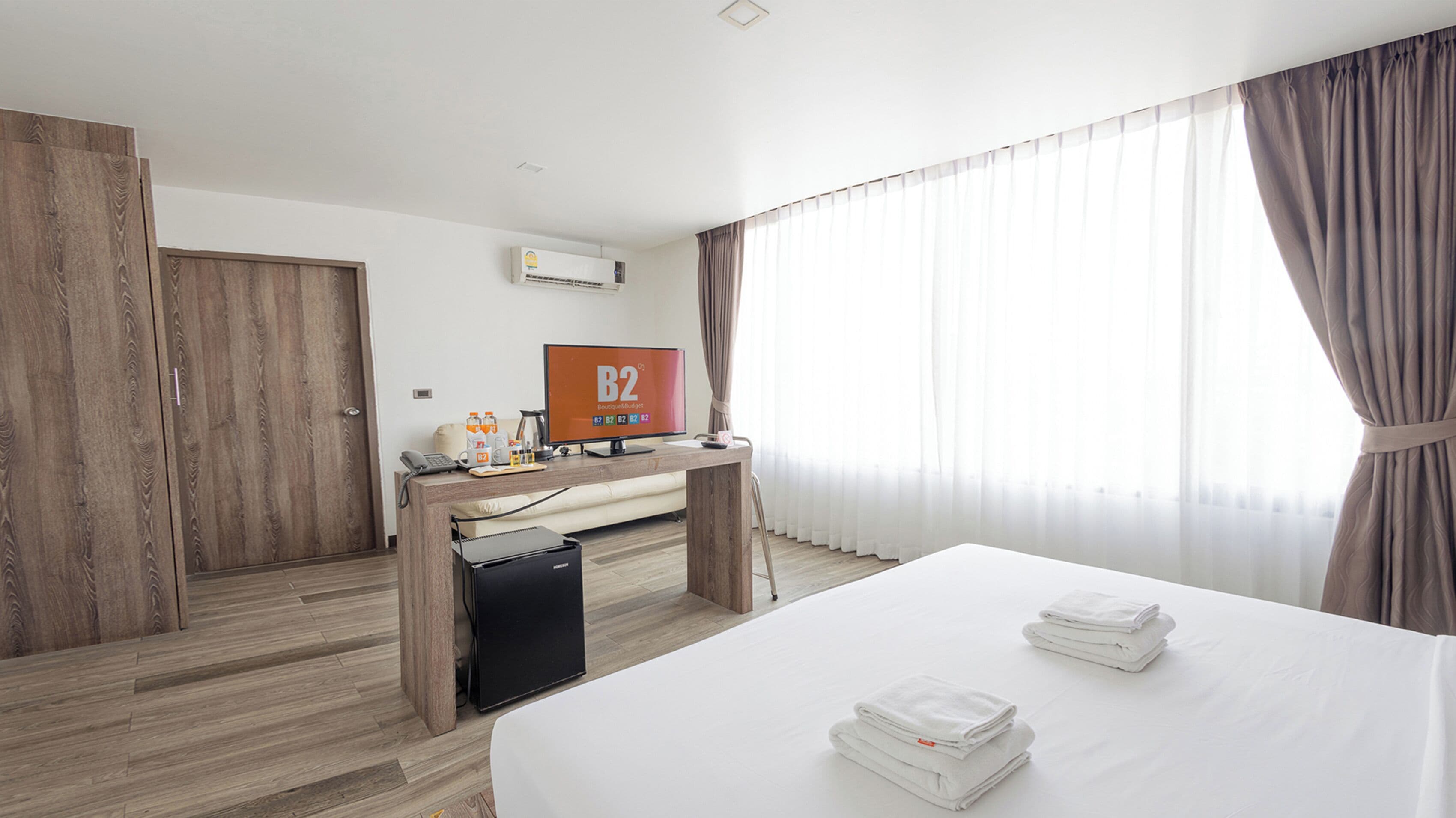 A hotel room with a bed, a desk with a computer, a TV, and a minibar.