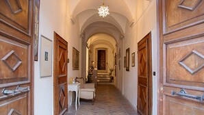 A hallway with wooden doors, a white table, and a chair, leading to a staircase. - Palazzo Meraviglia - Albergo Diffuso (Corinaldo)