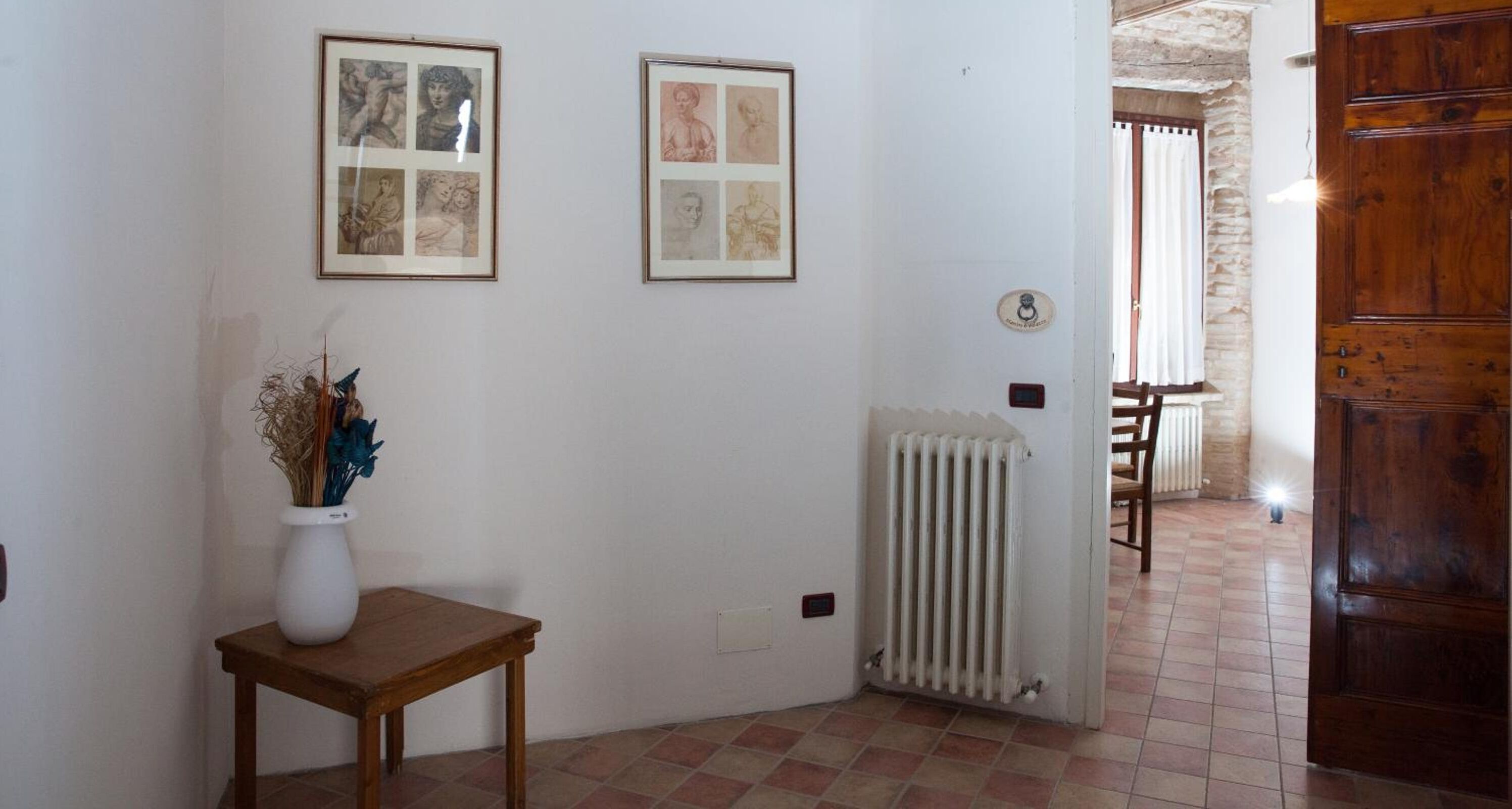 Un couloir avec deux œuvres d’art encadrées accrochées au mur, un radiateur et une porte en bois.