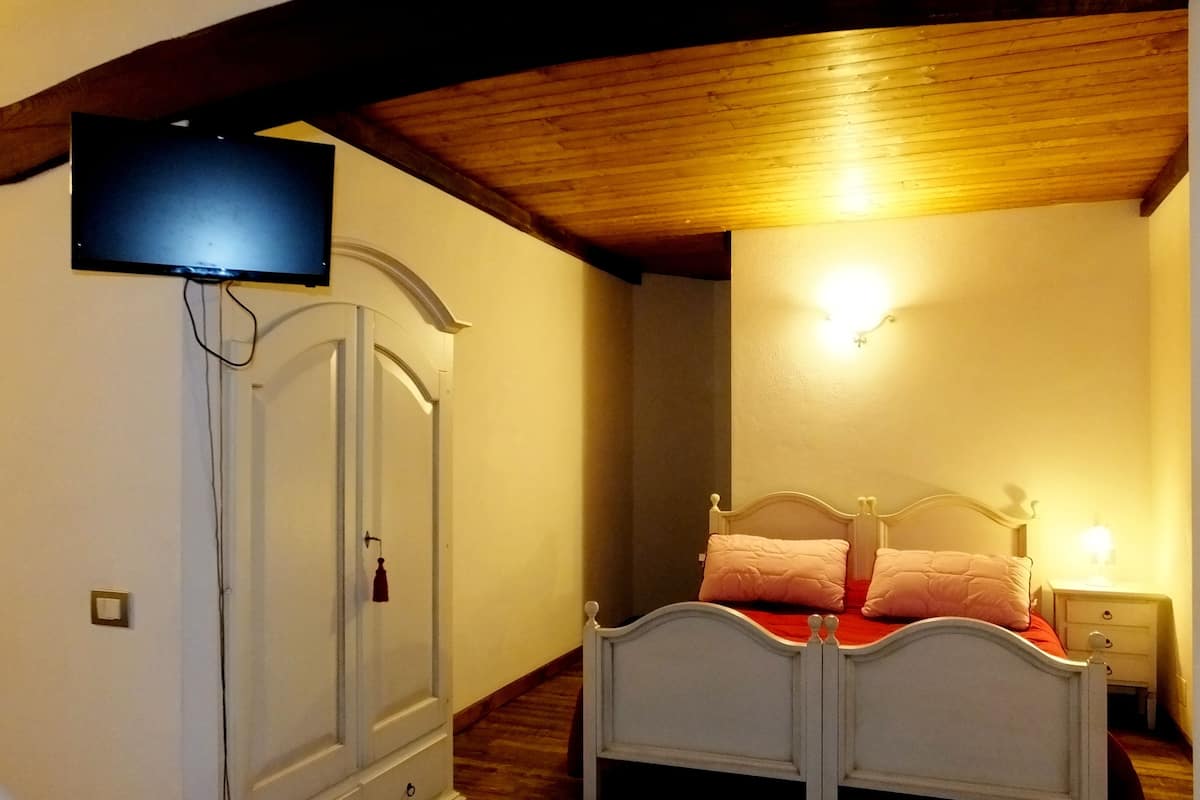 A bedroom with a wooden ceiling, a white wardrobe, a bed with white headboard, and a wall-mounted TV.