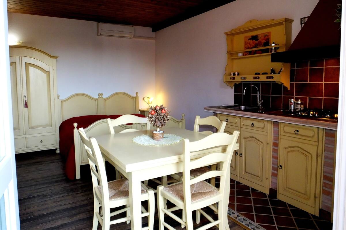 A dining area with a table and chairs, a kitchen with a stove and sink, and a wardrobe.