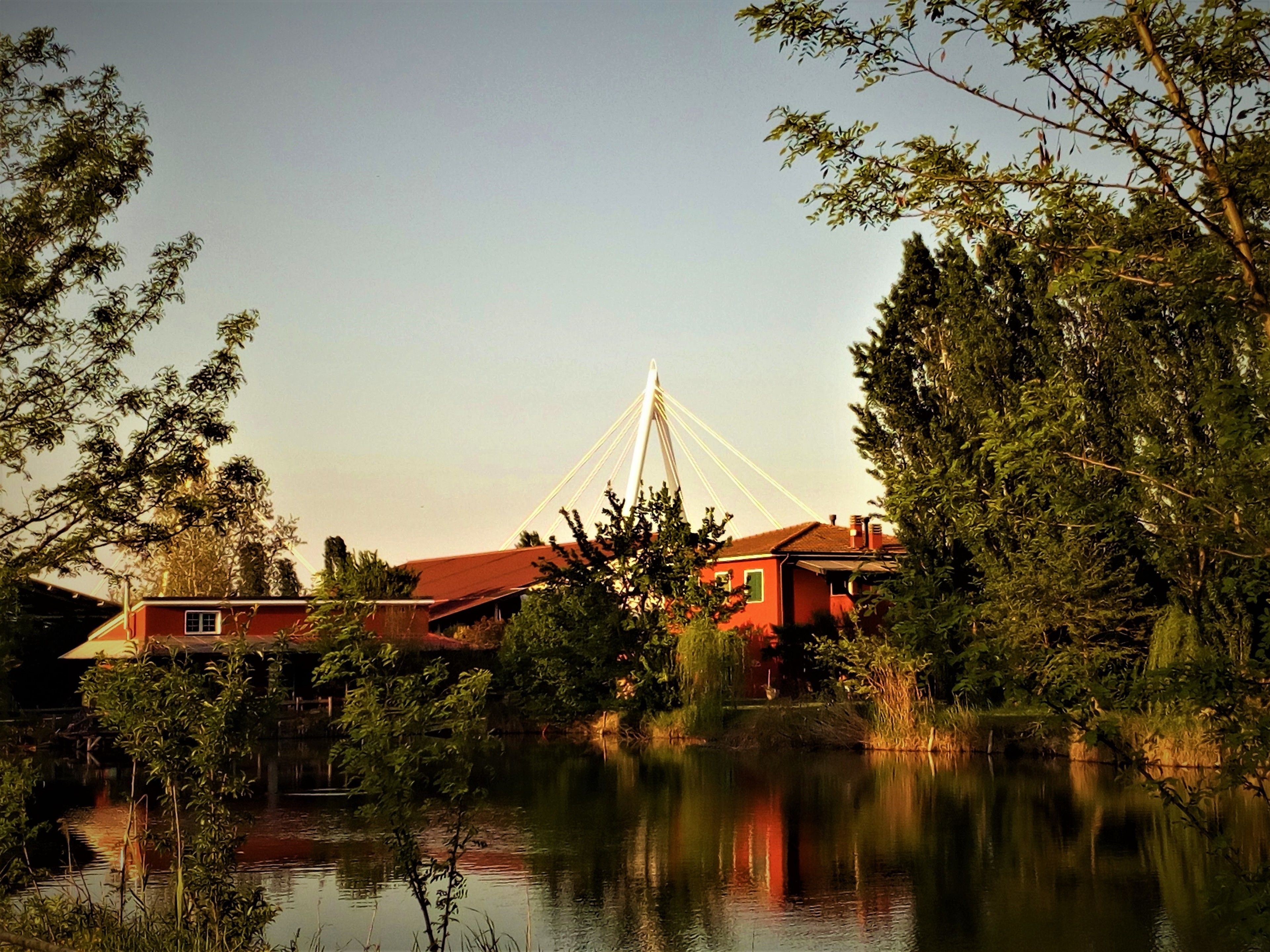 A house with a red roof, surrounded by trees and a body of water.