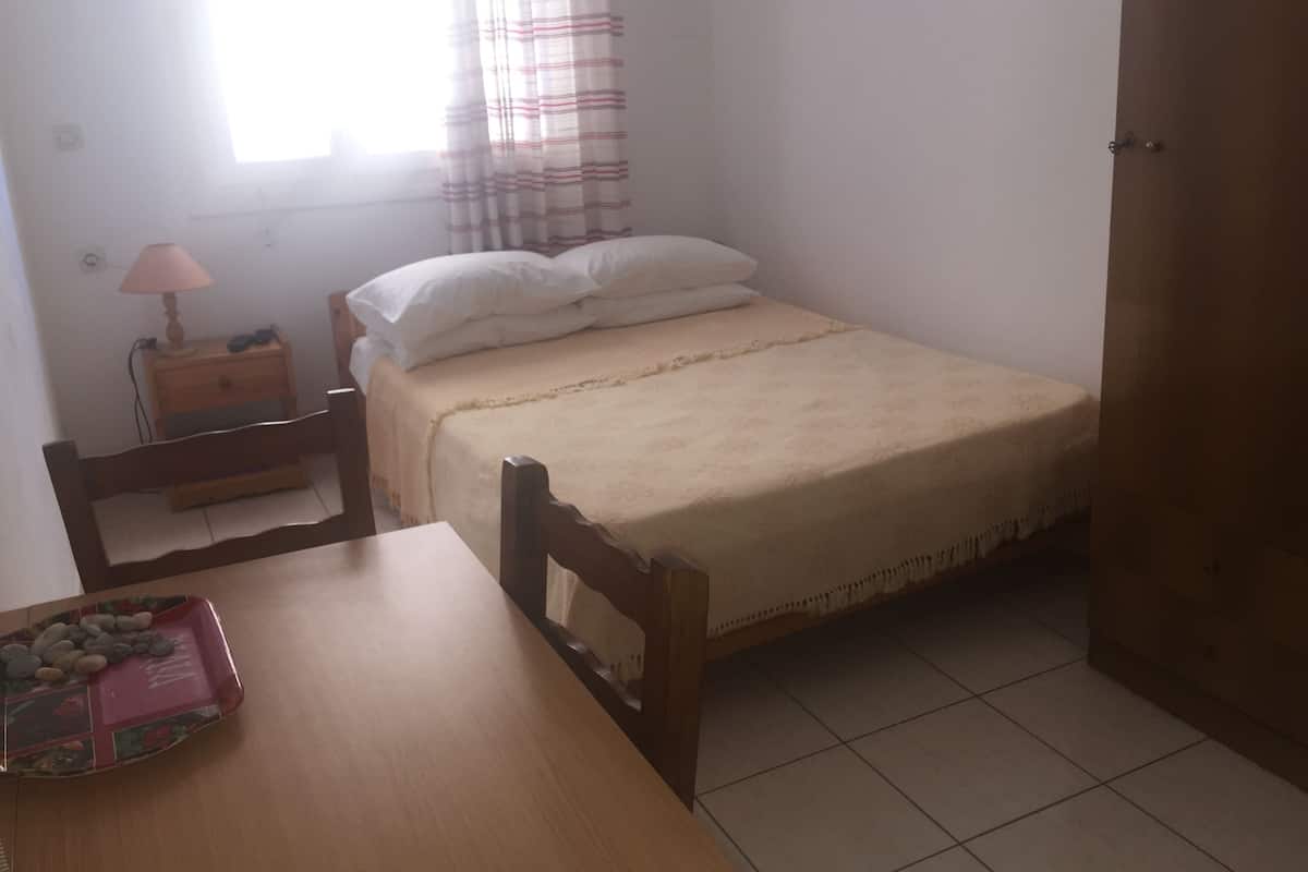 A bedroom with a bed, a bedside table with a lamp, a wooden chair, and a small table with a decorative tray.