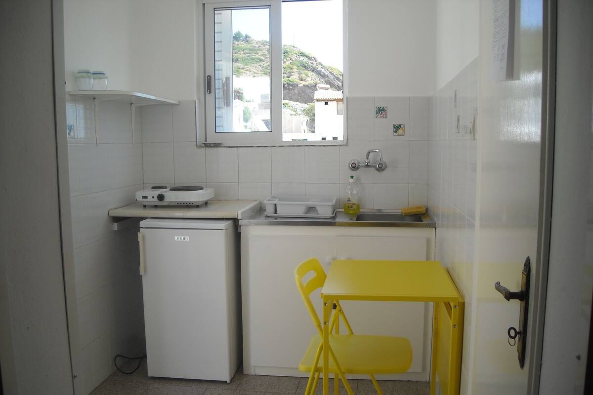 A compact kitchen with a small refrigerator, a sink, and a window.