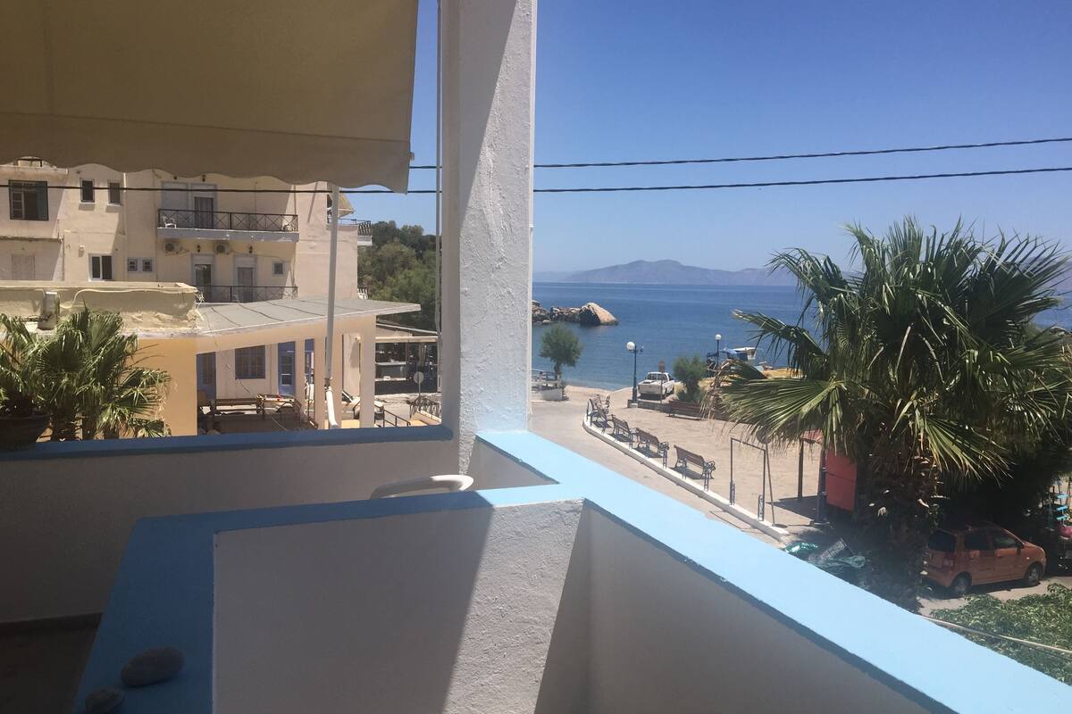 A balcony with a view of a coastal area, including buildings, a road, and a car.