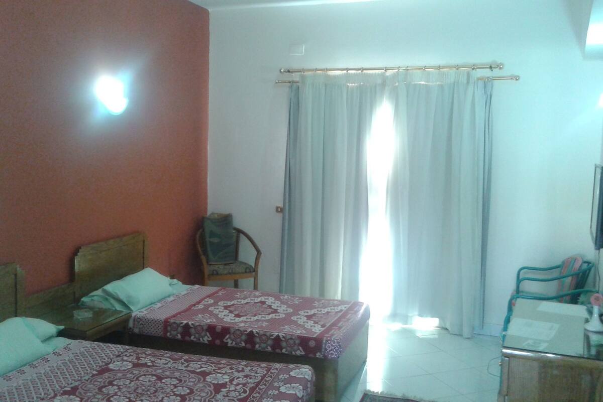A hotel room with two beds, a chair, a desk, and a window with curtains.