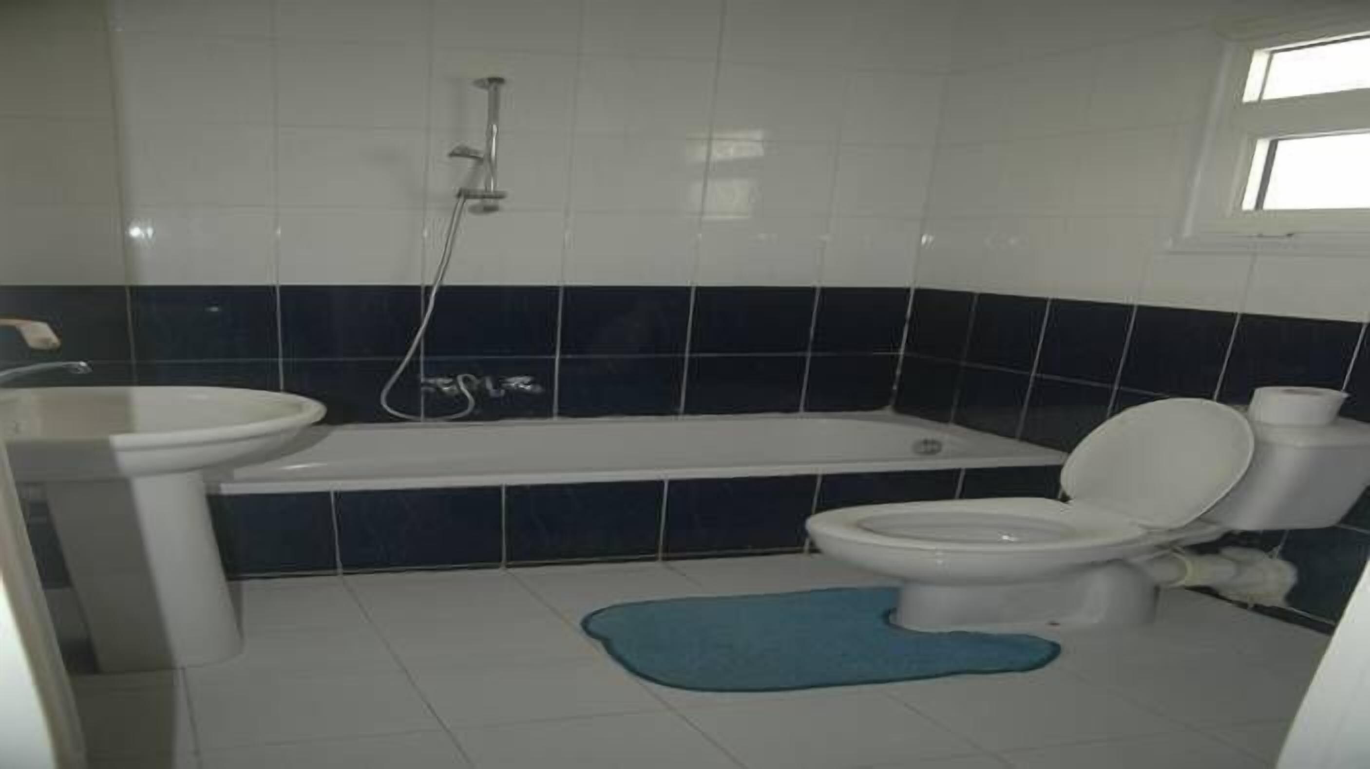 Un baño con bañera, inodoro, lavamanos y una alfombra de baño azul.