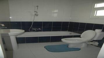 Un baño con bañera, inodoro, lavamanos y una alfombra de baño azul.
