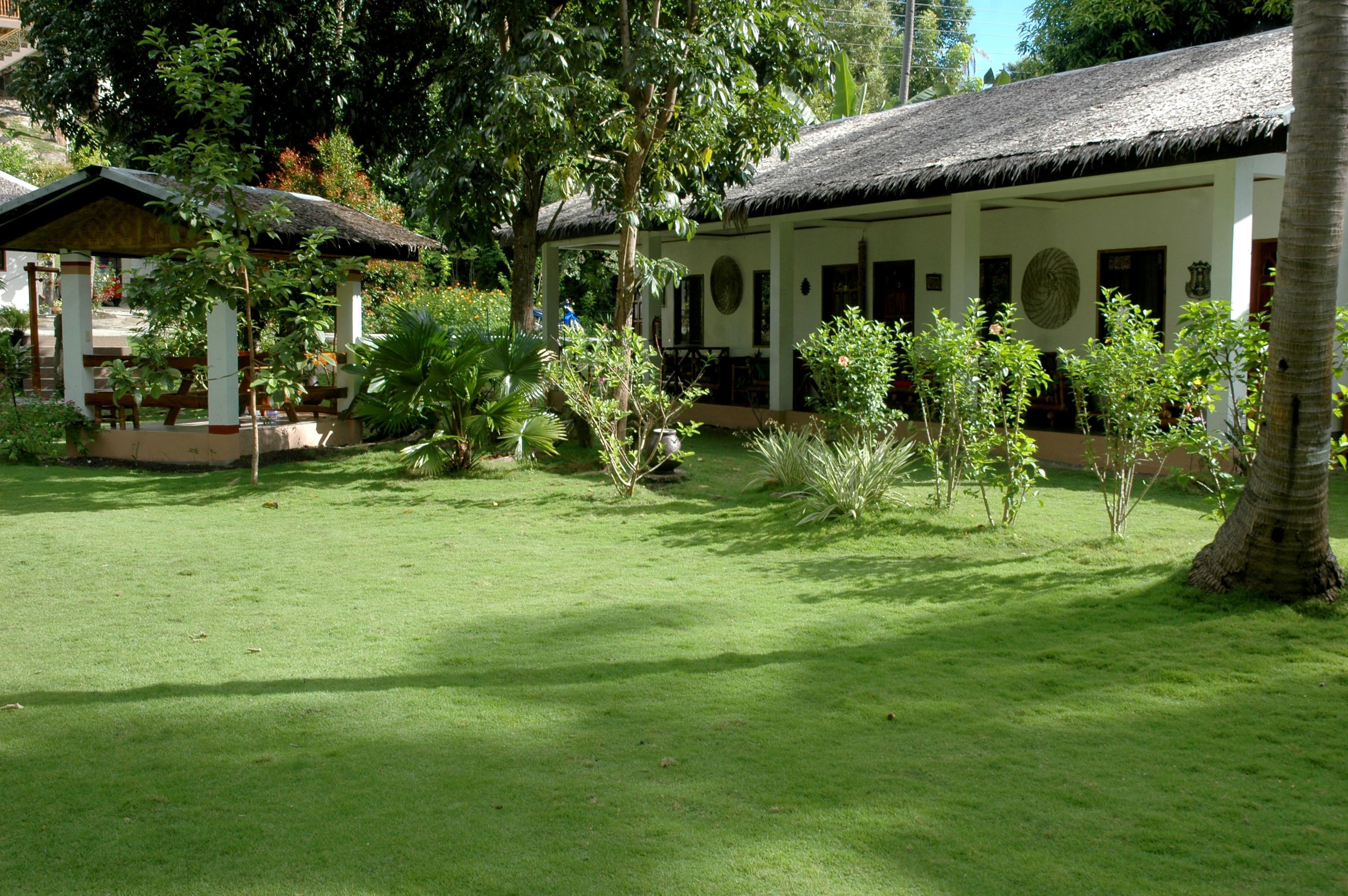 A well-maintained garden with a thatched-roof building, surrounded by lush greenery and palm trees.