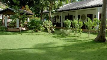 A well-maintained garden with a thatched-roof building, surrounded by lush greenery and palm trees.