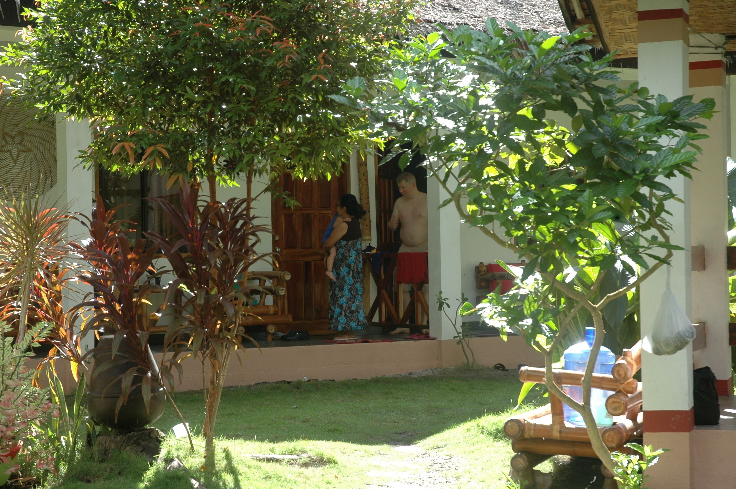 A covered outdoor area with a wooden bench, a large potted plant, and a small table.