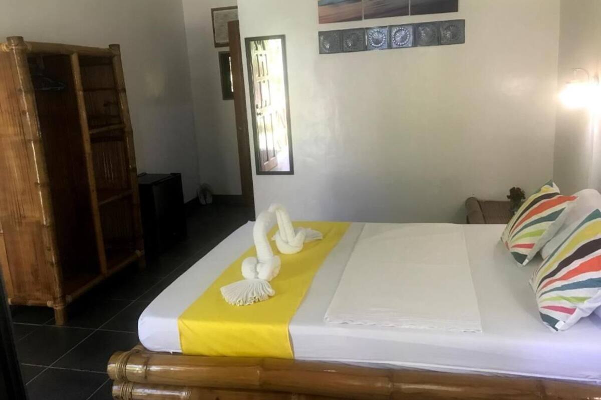 Una cama bien hecha con un detalle amarillo, un armario de madera y una pared con cuadros.