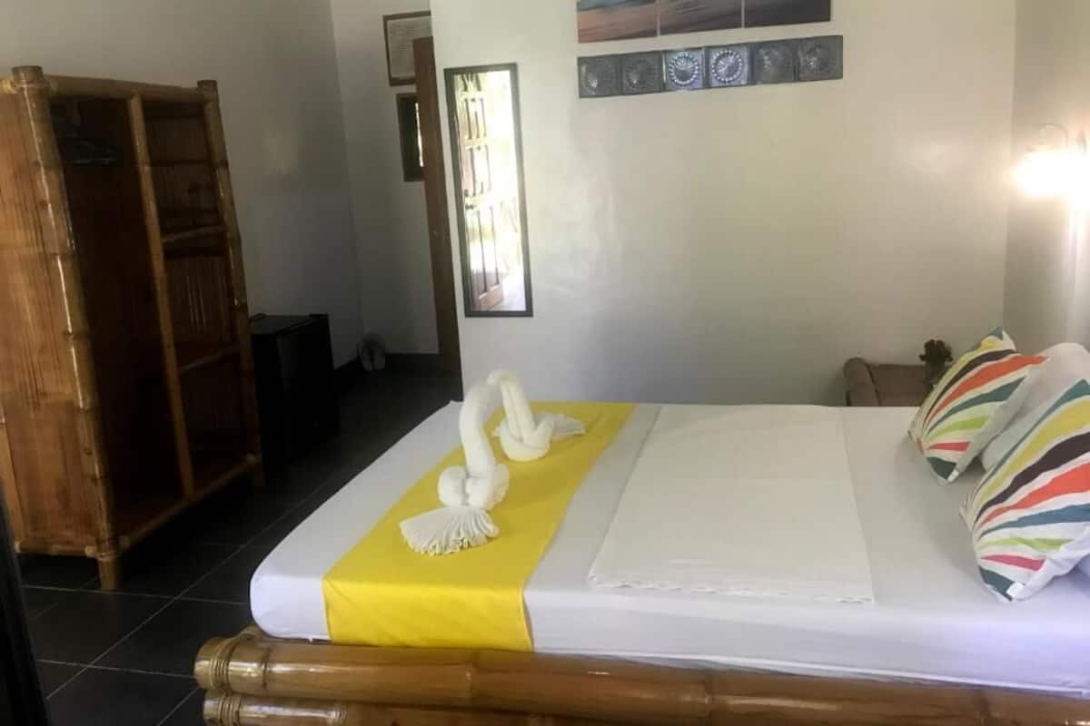 Una cama bien hecha con un detalle amarillo, un armario de madera y una pared con cuadros.
