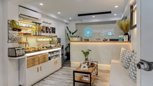 A modern reception area with a counter, a coffee station, and a seating area with a sofa and decorative plants. - Margaret of Naxos (Naxos)