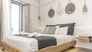 A modern bedroom with a wooden bed, white bedding, patterned pillows, and a bedside table with a lamp. - Margaret of Naxos (Naxos)