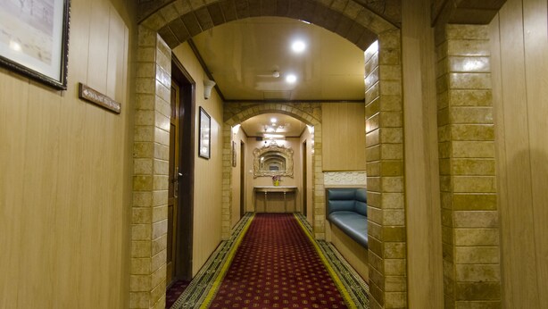 A hallway with a red carpet, stone walls, and a bench on the right. - Hotel Days Inn (Karachi)