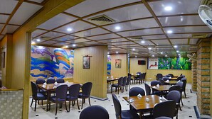 A restaurant with a tiled floor, wooden panel walls, and a mural. There are tables and chairs arranged for dining. - Hotel Days Inn (Karachi)