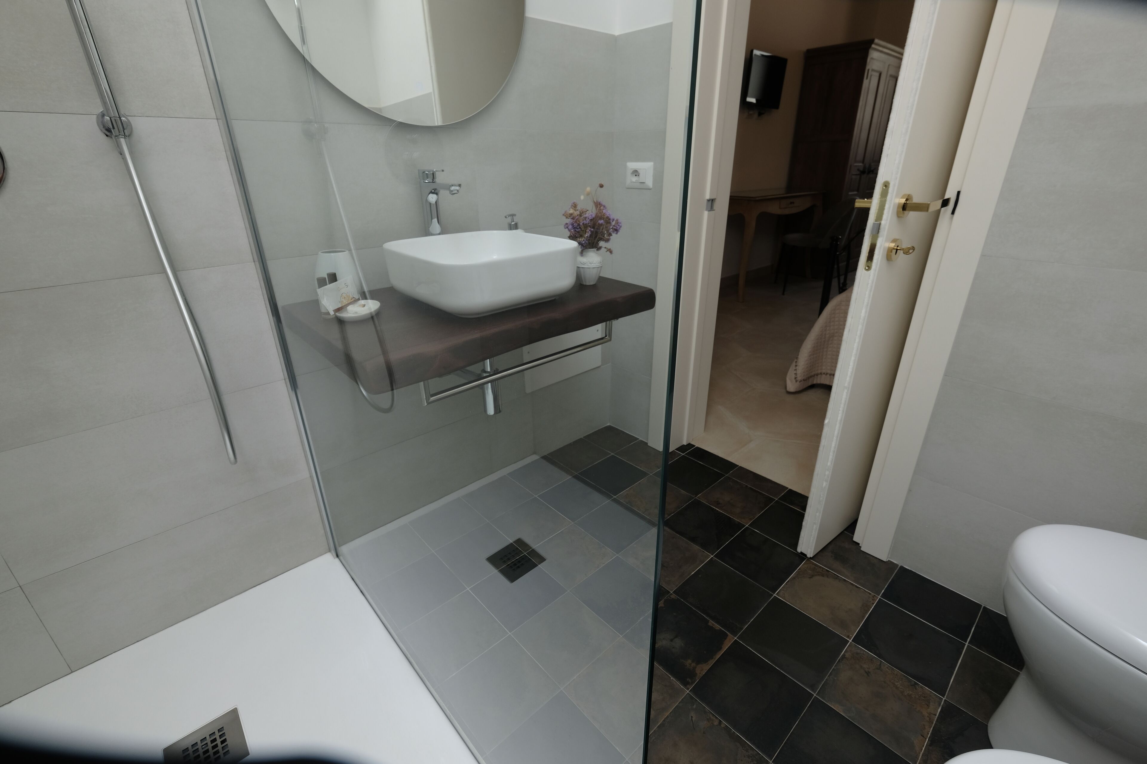 Une salle de bain moderne avec une douche à parois de verre, un lavabo blanc doté d’un plan de toilette foncé et des toilettes.