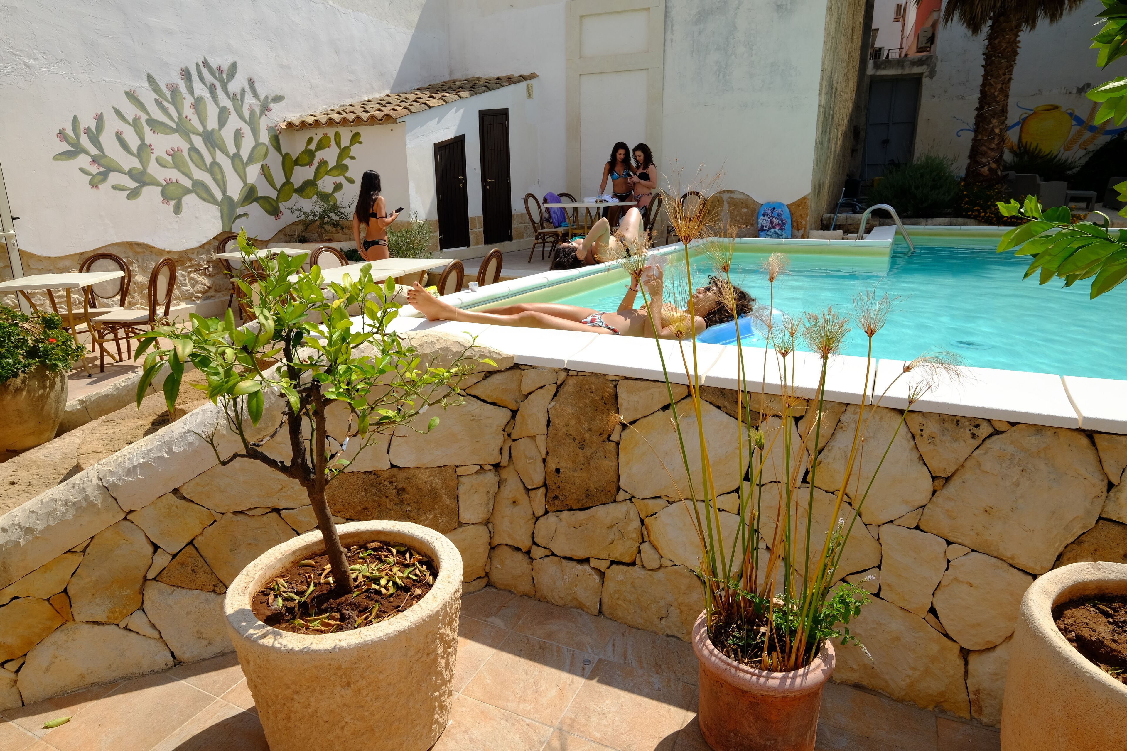 Un espace piscine agrémenté de murs en pierre, de plantes en pot et de mobilier d’extérieur.