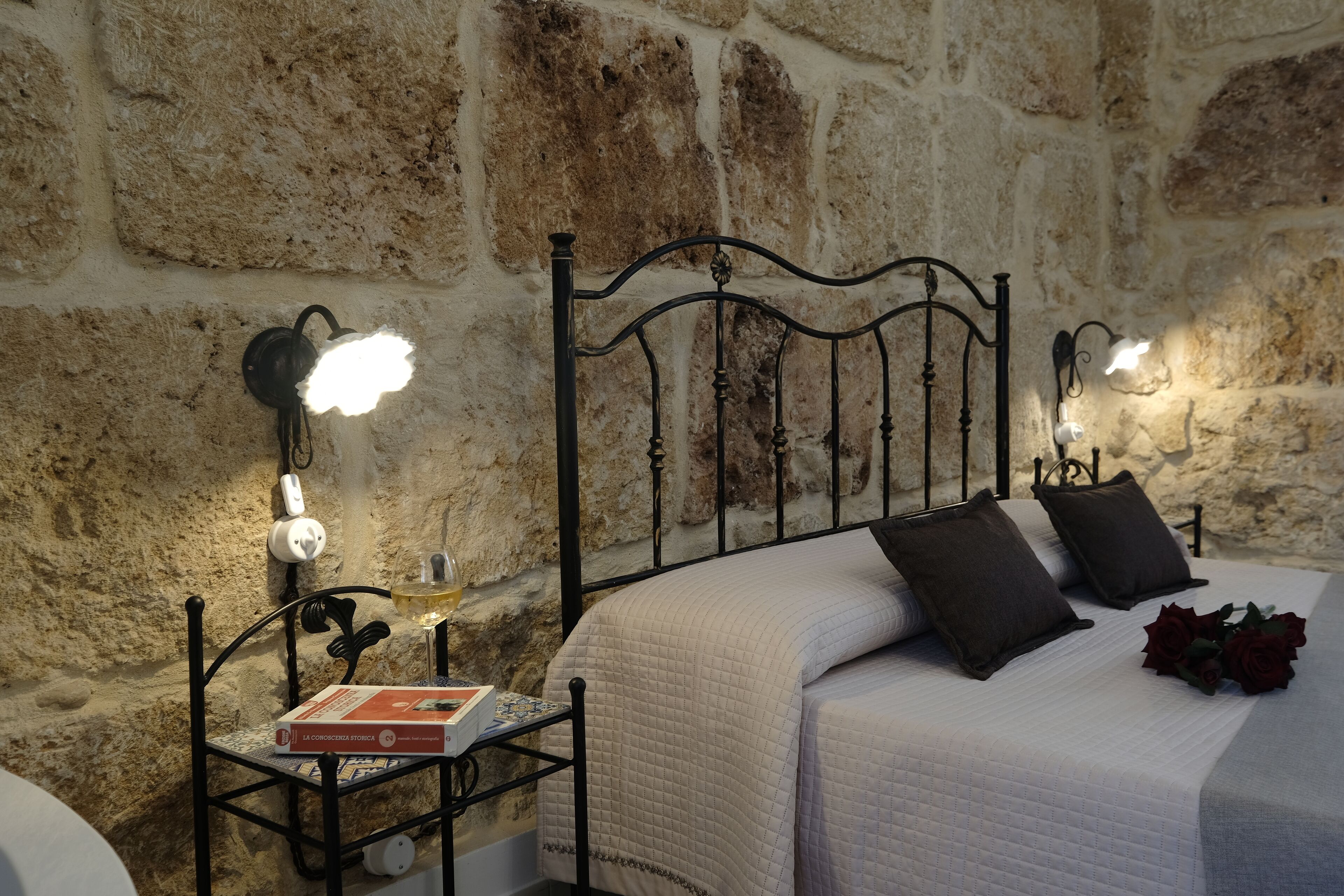 A bedroom with a stone wall, a metal bed frame, and bedside lamps.